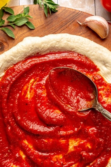 Spoon spreading pizza sauce on pizza dough.