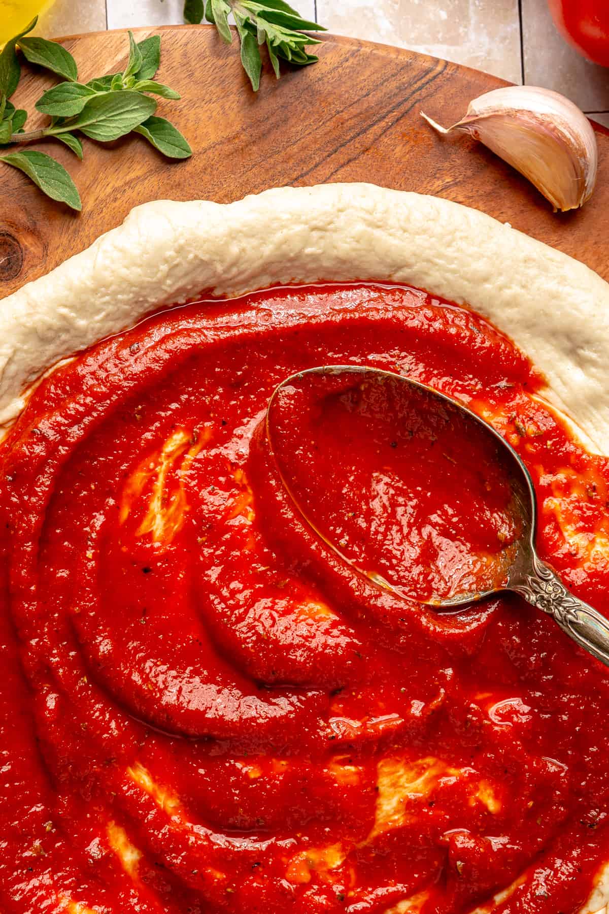 Spoon spreading pizza sauce on pizza dough.