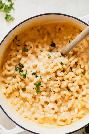 Dutch oven filled with creamy Mac and cheese with wooden spoon to serve.