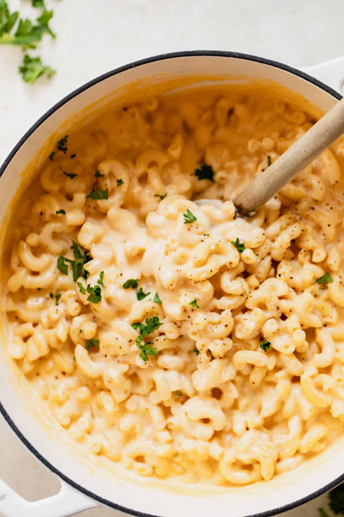 Dutch oven filled with creamy Mac and cheese with wooden spoon to serve. 