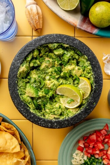 Molcajete with guacamole topped with lime wedges.