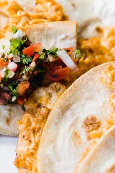 Tray filled with baked chicken quesadillas topped with fresh Pico de Gallo and extra sour cream.