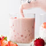 Fresh homemade agua de fresas with cream being poured into a cup with ice.