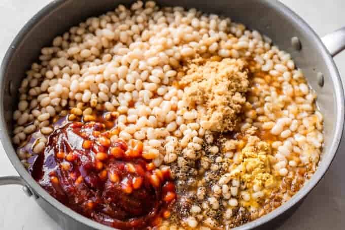 Large skillet filled with beans, topped with seasoning, molasses, bbq sauce, and brown sugar.