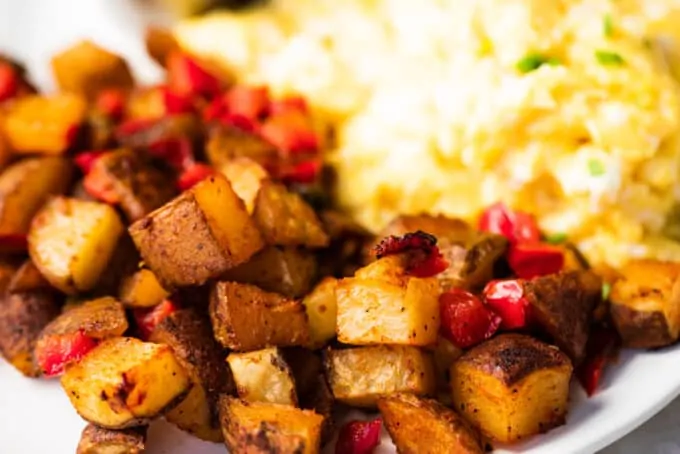 Breakfast potatoes served on a white plate next to some soft scrambled eggs.