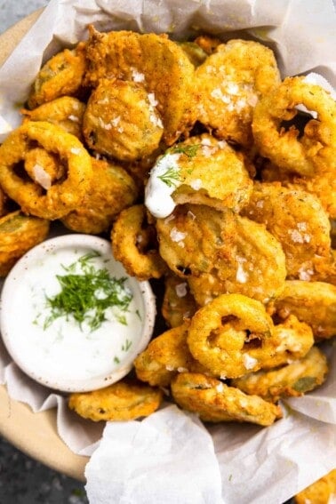 Basket of fried pickles with fried jalapeños and a bowl of ranch topped with fresh herbs.