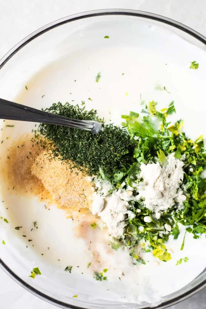 Small glass bowl filled with a white creamy sauce and topped with fresh herbs and seasonings. 