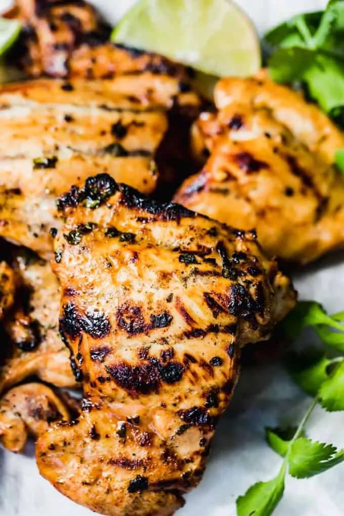 Pile of grilled chicken breast with a sprinkle of cilantro on the side and lime wedges.