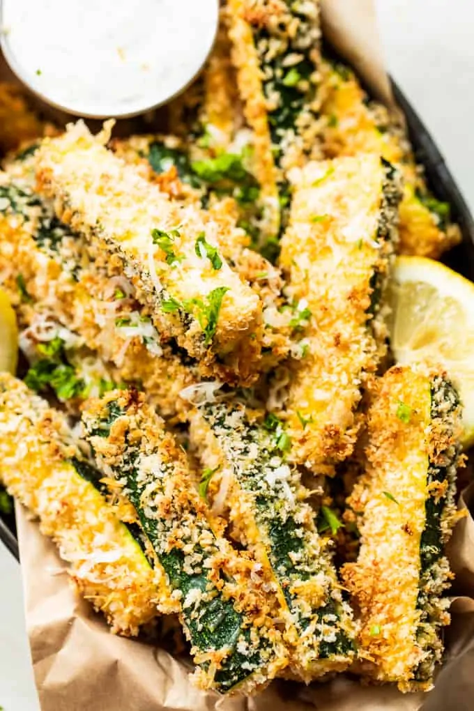 Basket filled with zucchini fries, showing a cup of ranch dressing and a lemon wedge on the side.