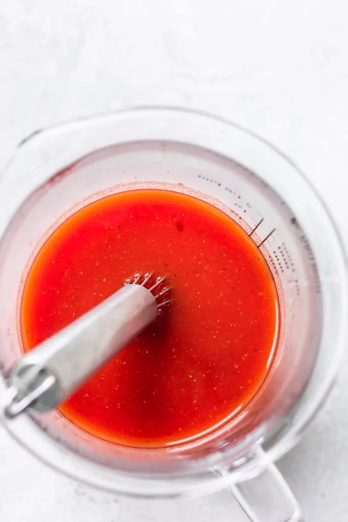 Measuring glass filled with homemade Clamato juice, with a whisk.