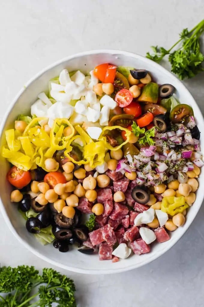 A white bowl filled with green lettuce and topped with all the add-ins for an Italian chop salad.