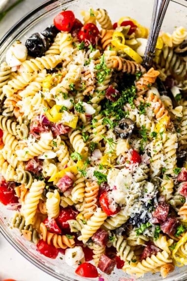 Close up view of rotini noodles with tomatoes, olives, salami, mozzarella, pepperoncinis, and shredded parmesan and fresh parsley, coated in Italian dressing.