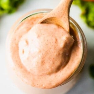 Overhead view of a wooden spoon scooping up burger sauce from a small glass jar.