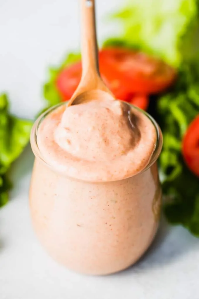 Wooden spoon scooping up burger sauce from a glass jar. 