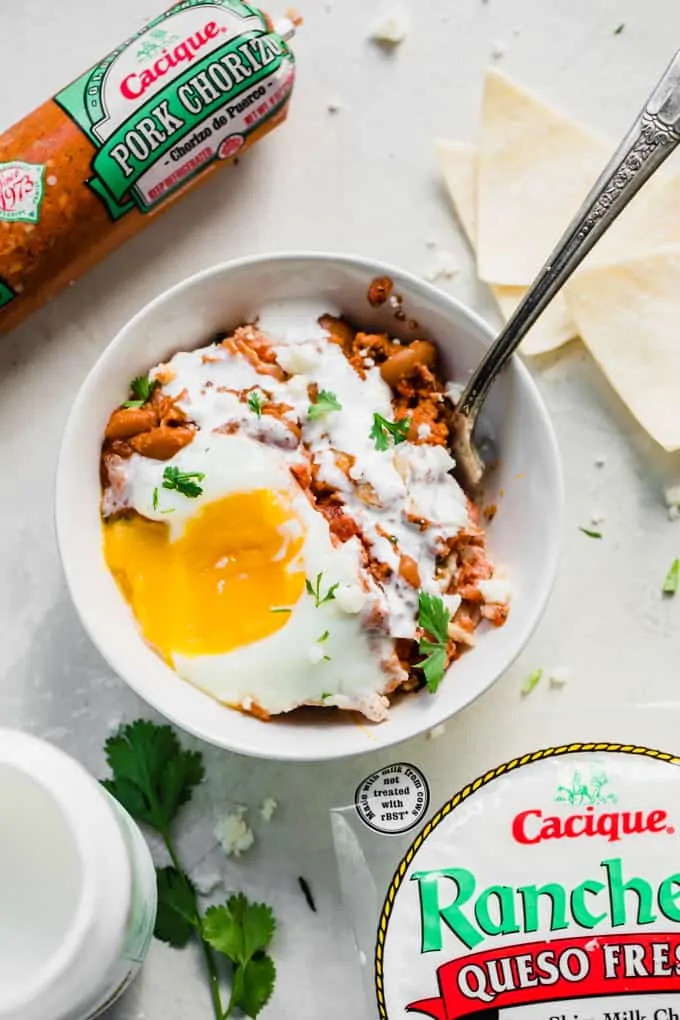 Bowl filled with huevos rancheros breakfast casserole, the egg broken and oozing, garnished with cilantro and a drizzle of Crema.