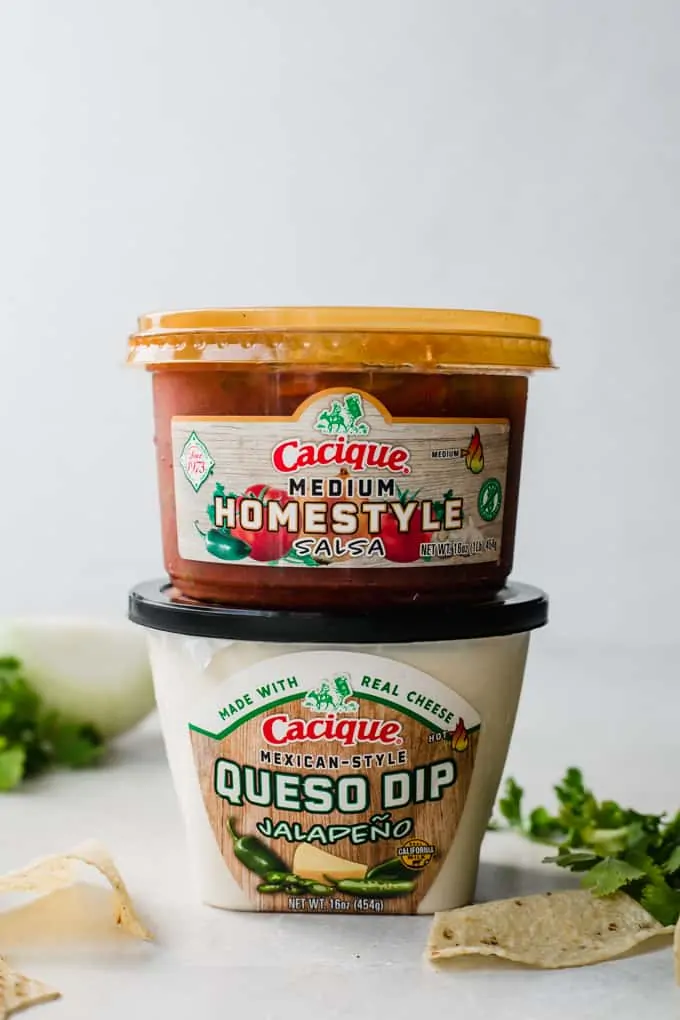 Stacked containers of Cacique brand Medium Homestyle Salsa and Mexican Style Queso Dip Jalapeno.