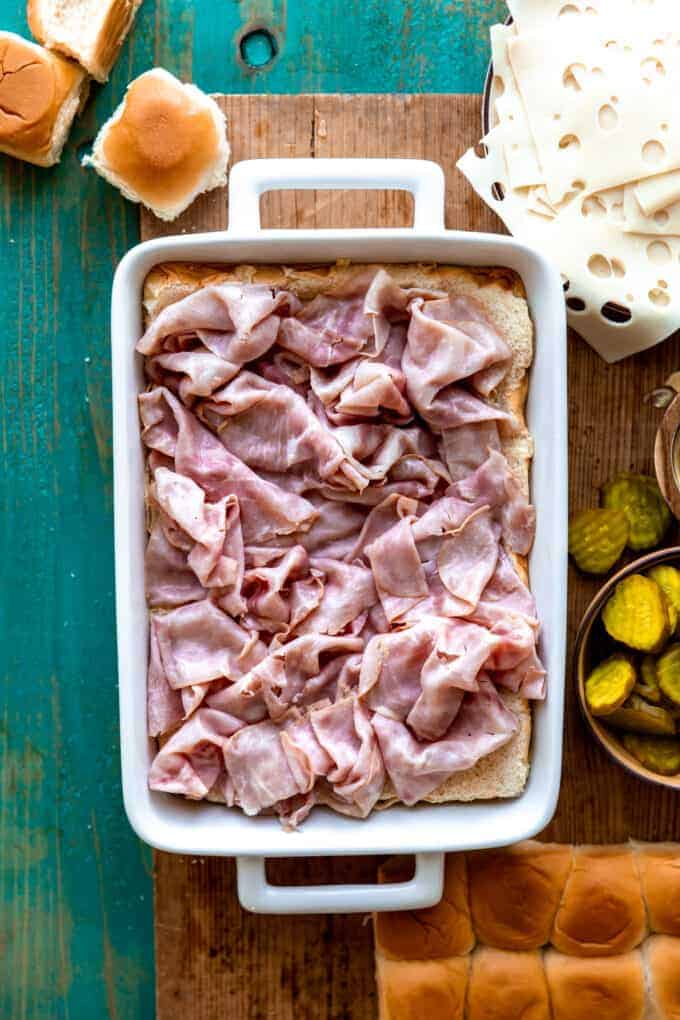 White baking dish filled with a layer of Hawaiian rolls topped with sliced deli ham.