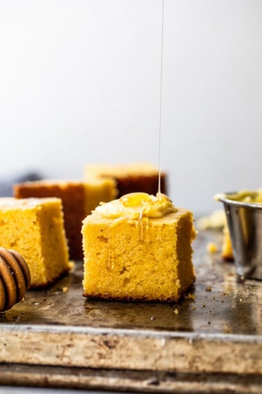 Slice of buttermilk cornbread with butter on top being drizzled with honey.