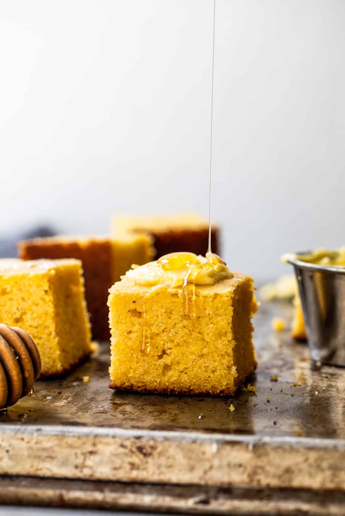 Slice of buttermilk cornbread with butter on top being drizzled with honey. 