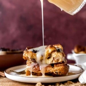 Vanilla syrup pouring over the top of a piece of bread pudding with raisins.