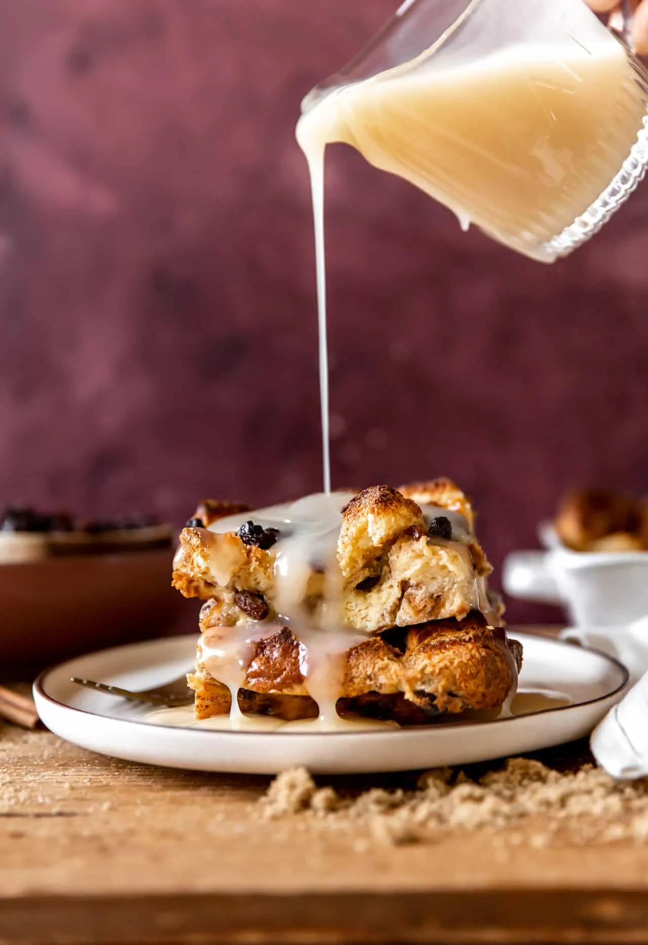 Vanilla syrup pouring over the top of a piece of bread pudding with raisins. 