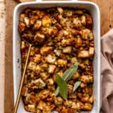 Dish with baked cornbread dressing topped with fresh sage leaves.