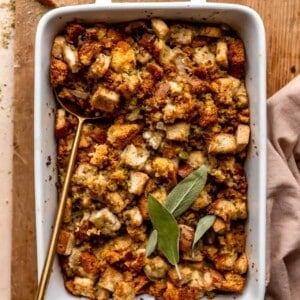 Dish with baked cornbread dressing topped with fresh sage leaves.