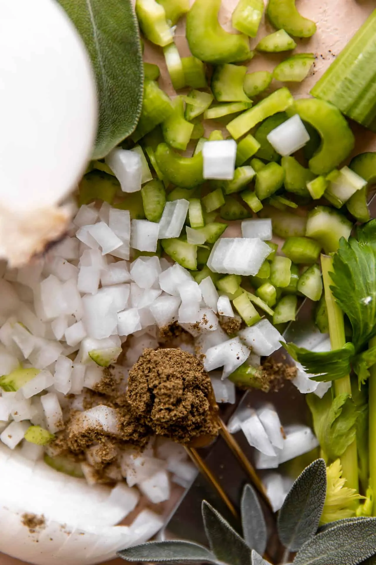 Ingredients needed to make homemade cornbread dressing. Sliced celery, onion, dried herbs, fresh herbs.