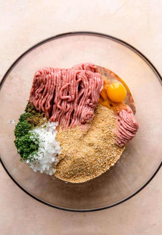 Ingredients for turkey meatballs in a glass bowl, ground turkey, bread crumbs, diced onion, egg and herbs and seasonings.