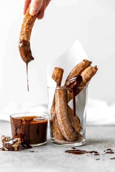 Churro being dipped into chocolate fudge.