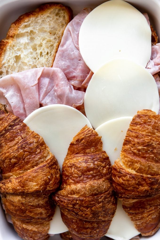 Layering croissants with ham and provolone for a breakfast casserole.