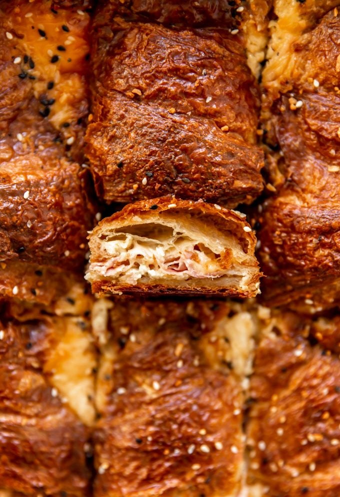 Croissant that has been cut showing flakey layers filled with melted provolone and layers of ham baked with egg custard for a breakfast casserole.