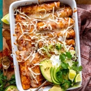 White baking dish filled with chicken enchiladas and topped with sliced avocado, sour cream and fresh cilantro.