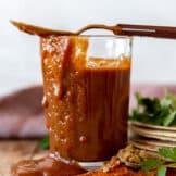 Cup filled with homemade enchilada sauce, with sauce dripping down the side and a spoon on top.