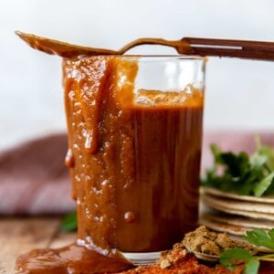 Cup filled with homemade enchilada sauce, with sauce dripping down the side and a spoon on top.