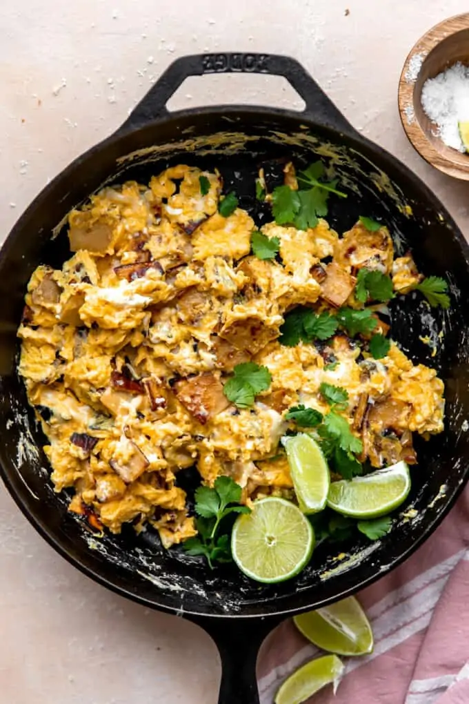Skillet with scrambled eggs and tortillas with fresh cilantro garnish and lime wedges.