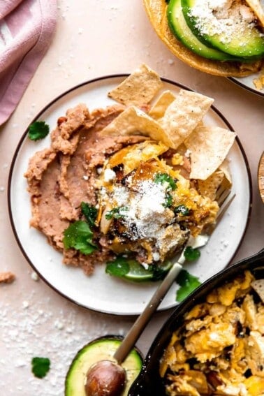 Overhead picture of Migas served over refried beans on a white plate.