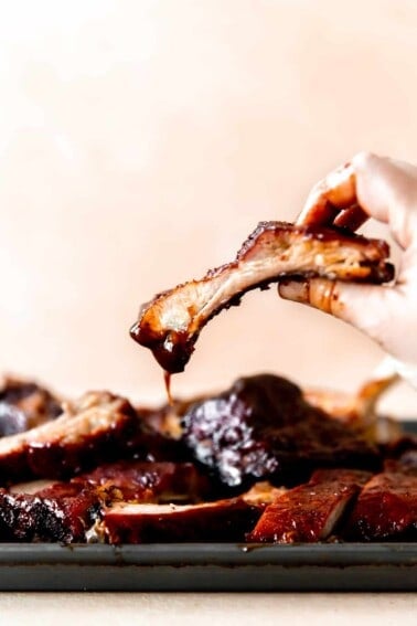 Hand picking up a smoked pork rib dipped in BBQ sauce.