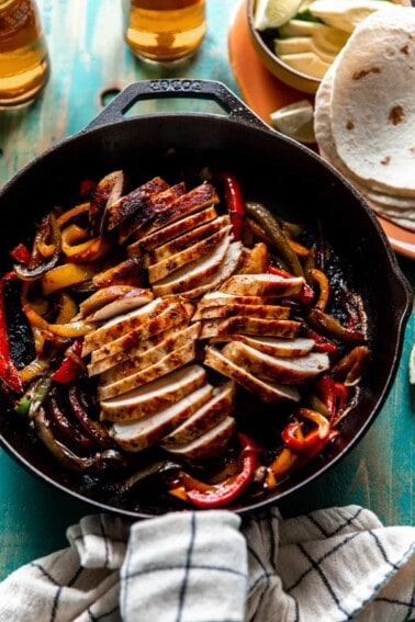 Skillet filled with chicken fajitas with beers and flour tortillas on the side.