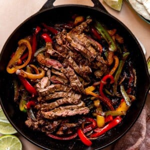 Large cast iron skillet filled with sliced grilled steak and grilled bell peppers and onions.