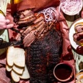 Texas Brisket on peach paper, sliced with slices of bread, cheese, pickles and onions around.