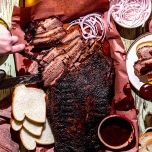 Texas Brisket on peach paper, sliced with slices of bread, cheese, pickles and onions around.