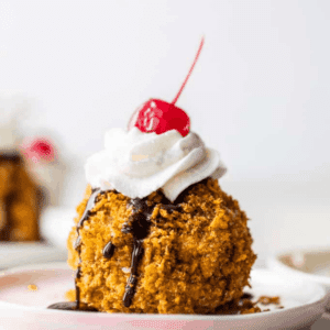 Fried Ice cream served on a plate, topped with whipped Cream and cherries