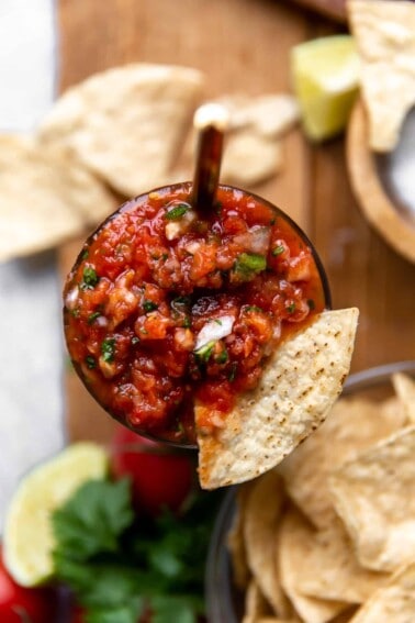 Overhead view of a jar of homemade sals with a tortilla chip being dipped in.
