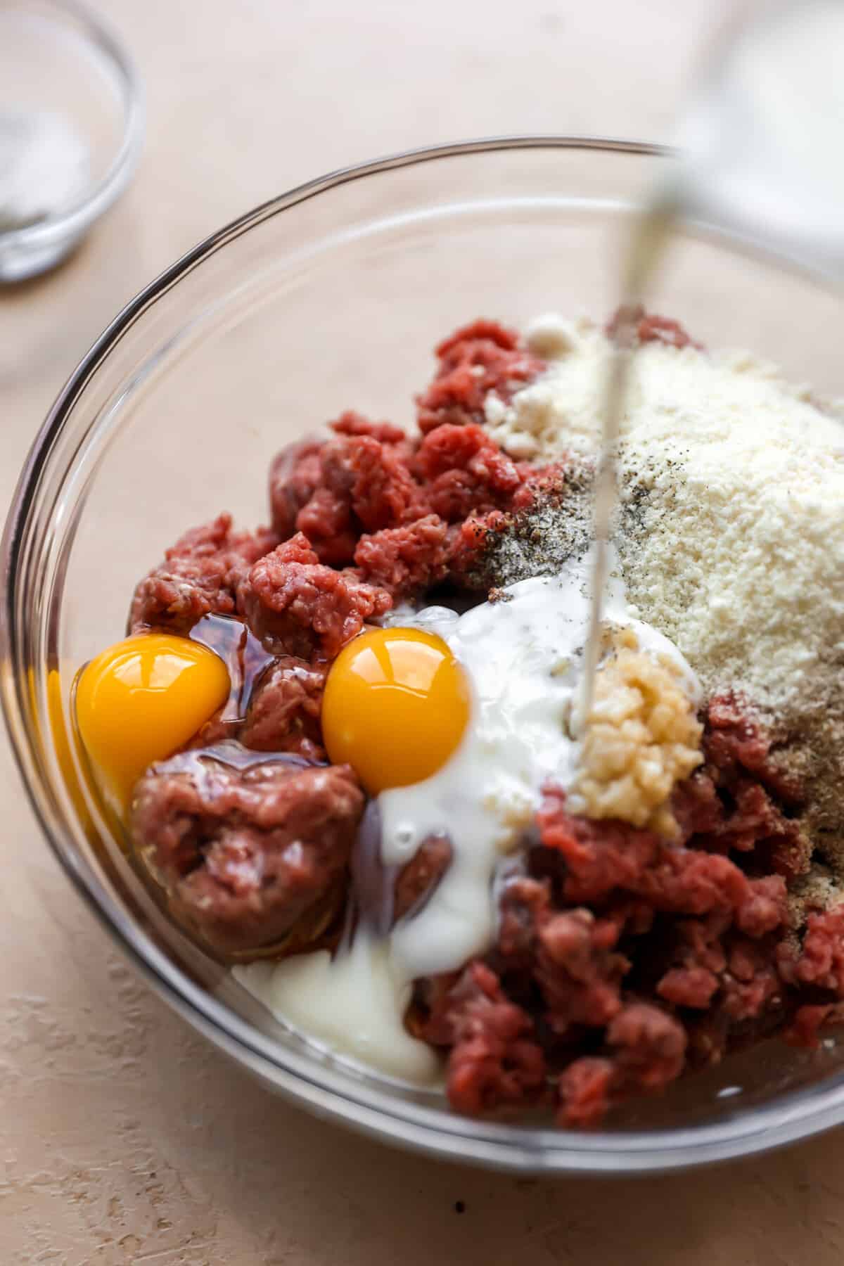 Milk pouring into meatball mixture in a glass bowl.