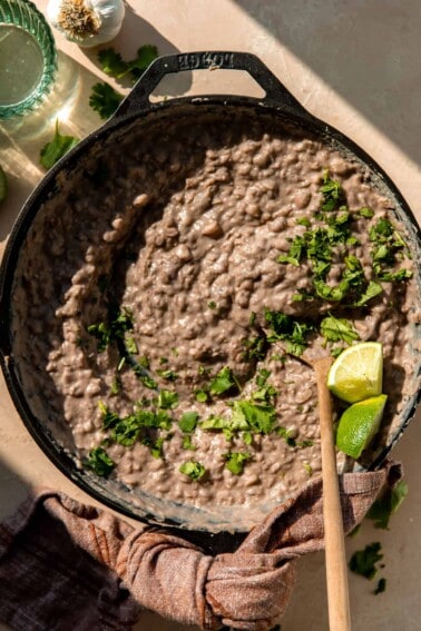 Skillet filled with refried beans, topped with cilantro and lime wedges.