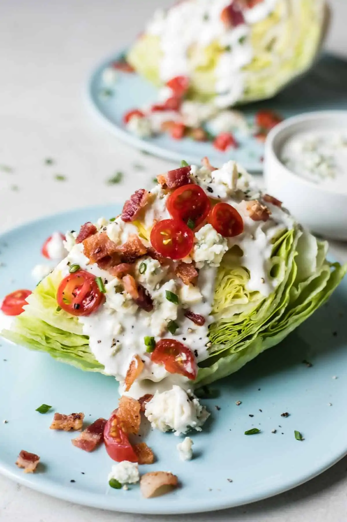 Wedge of lettuce on a blue plate topped with blue cheese dressing, tomatoes, bacon and chives.
