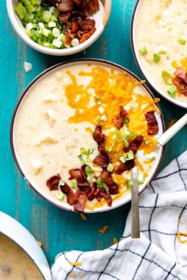 Bowl of potato soup topped with melted cheddar cheese, sour cream, diced bacon and green onion.