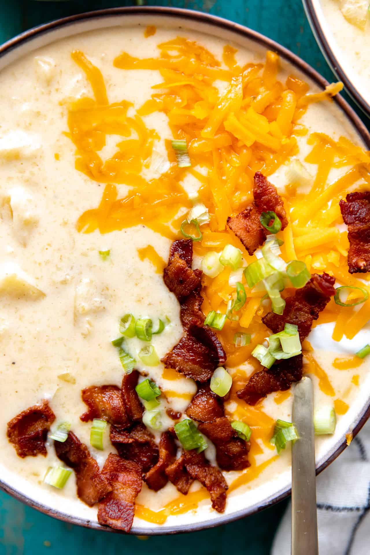 Up close view of potato soup in a bowl showing chunks of potato in a creamy broth, topped with bacon, cheese and green onion.