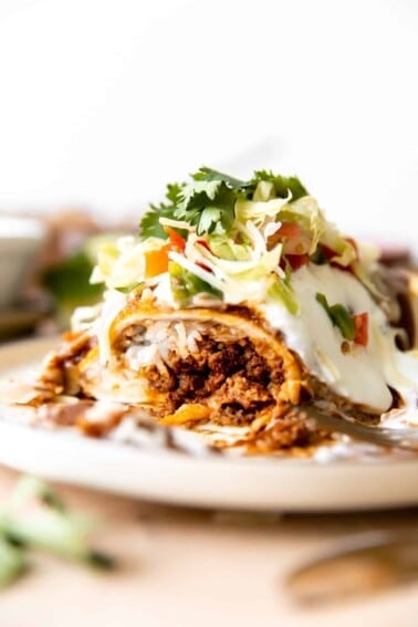 Wet burrito cut open to show it's filled with ground beef, cheese and rice. Topped with red sauce and sour cream.